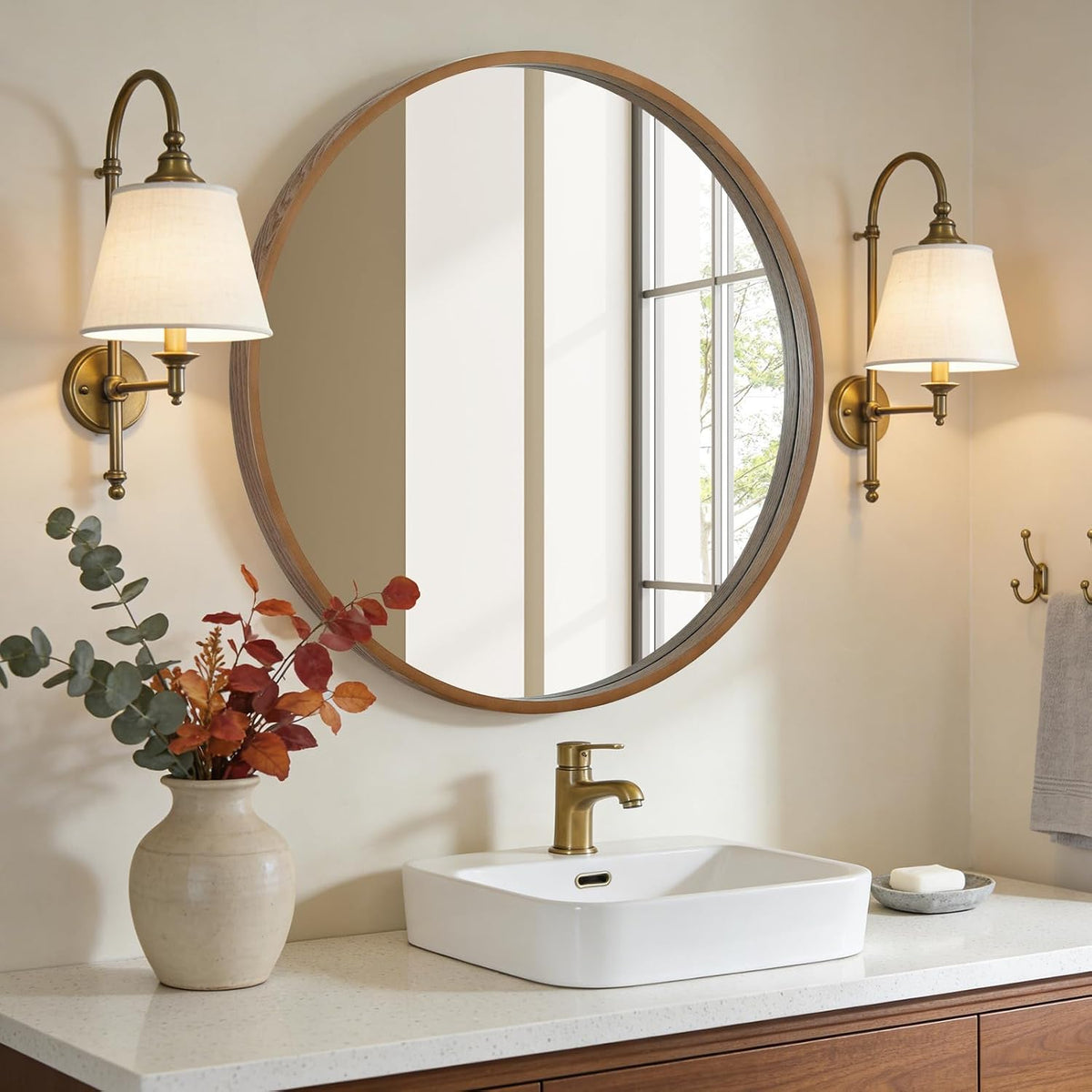 Natural wood round mirror over a bathroom vanity with sconces